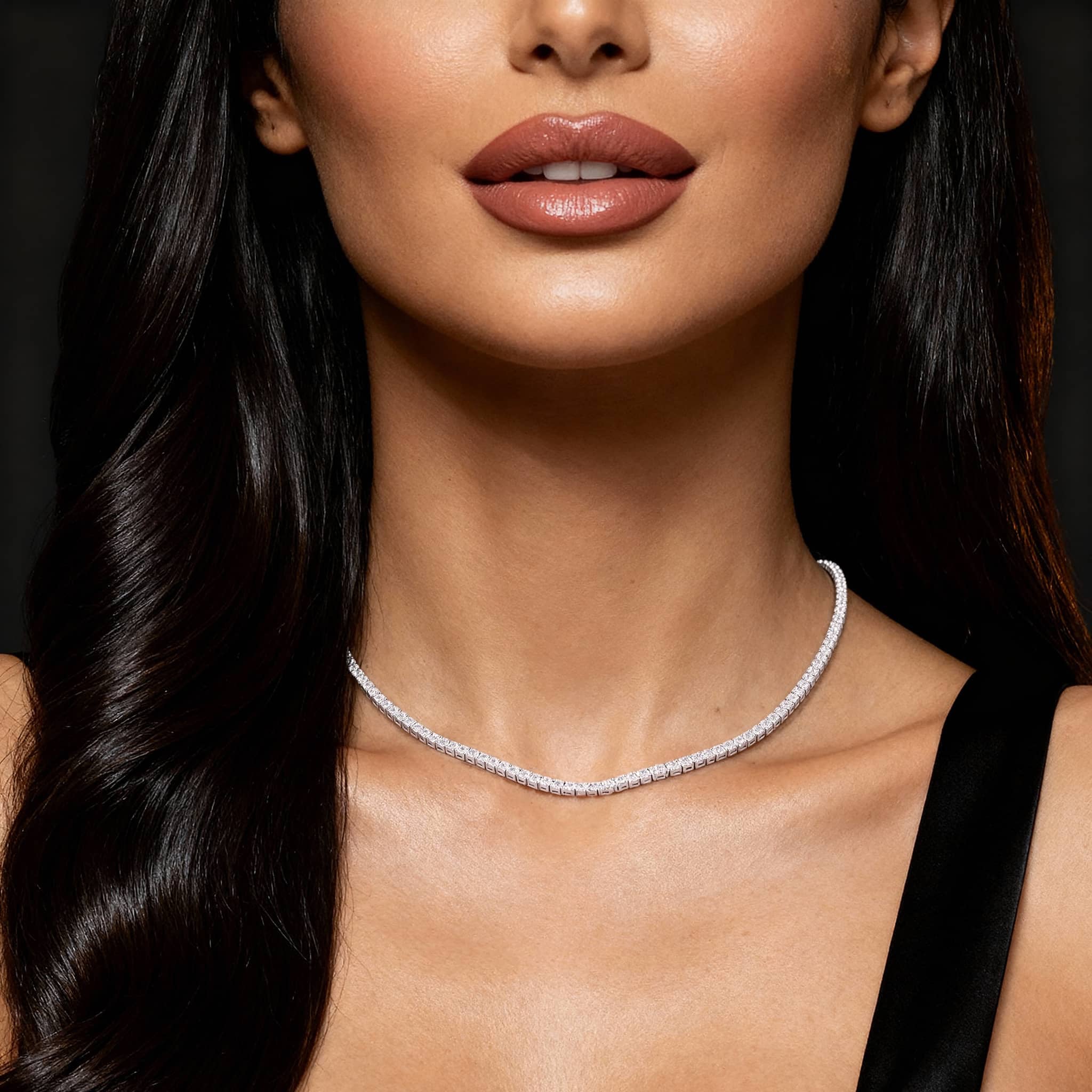 Close-up of a woman wearing a delicate necklace against a dark background